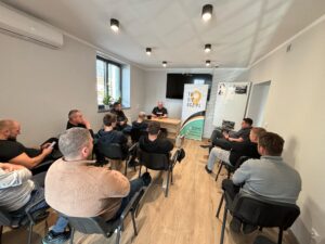 Sala wykładowa z kursantami i instruktorem, na trzecim planie roll-up reklamowy firmy TuSięUcz.pl